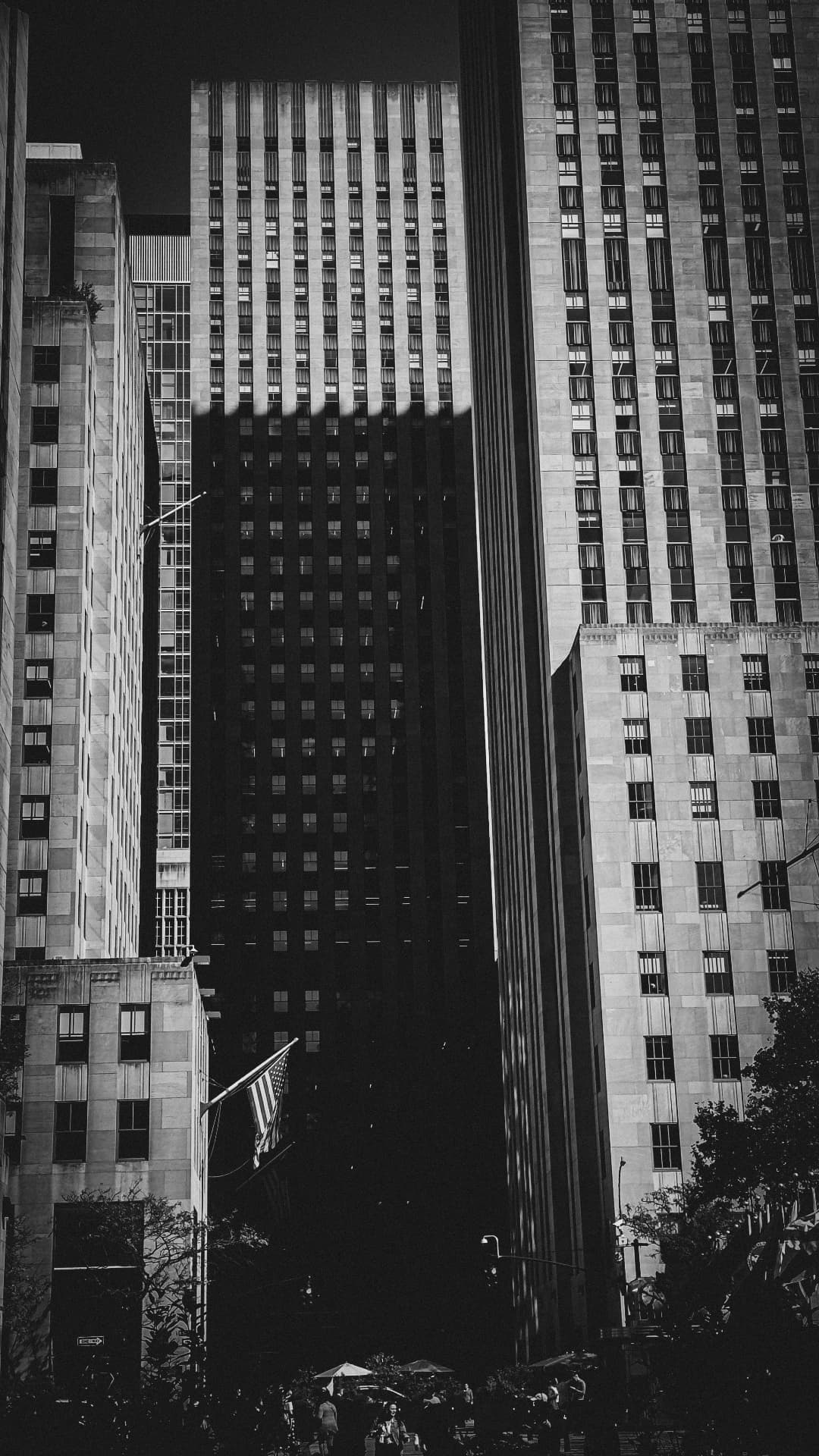 Black and white frame of Manhattan towers split by a deep central shadow above the street