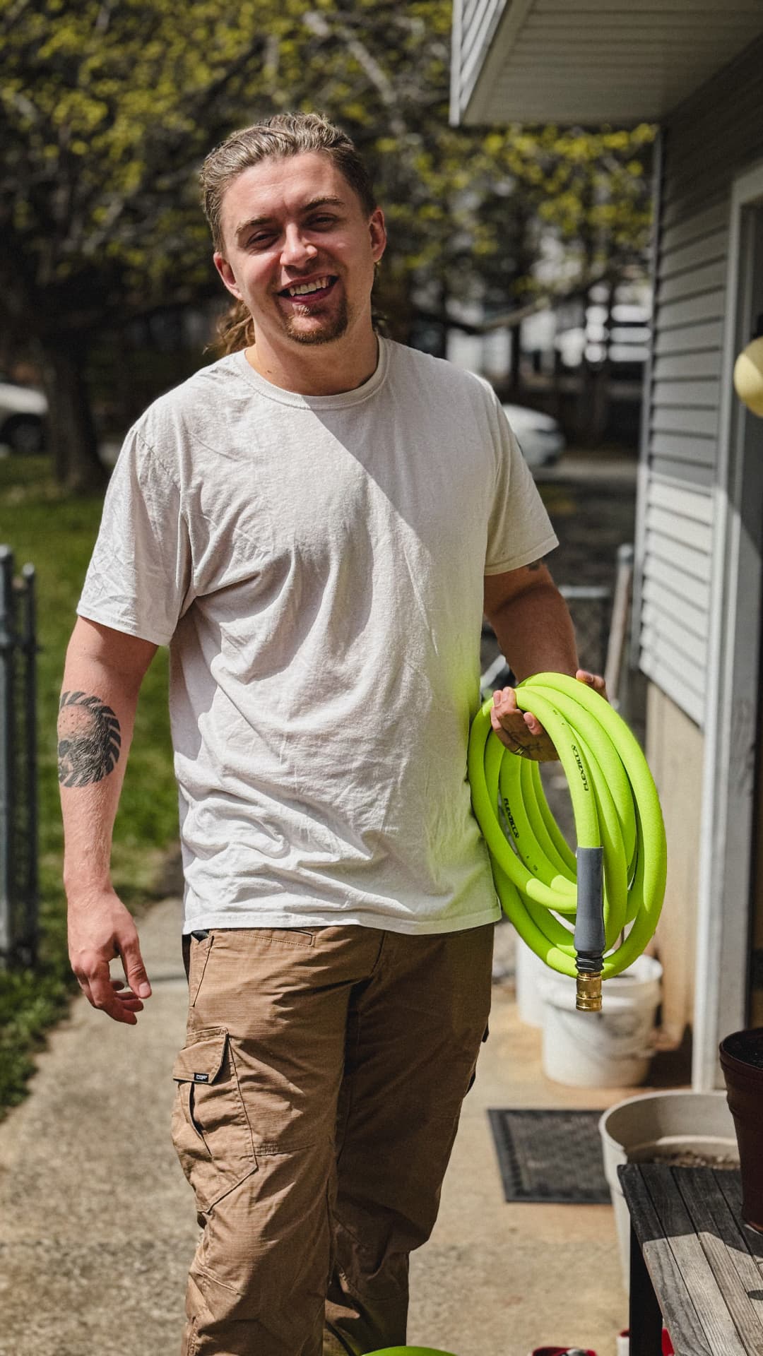 Outdoor cleaner standing beside a house holding a coiled bright green hose