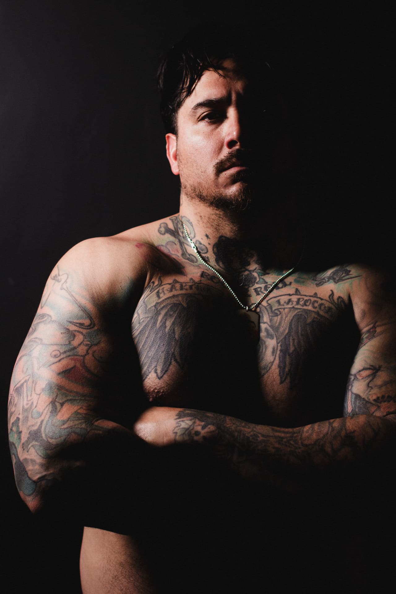 Dramatic low-key portrait of a tattooed man with arms crossed